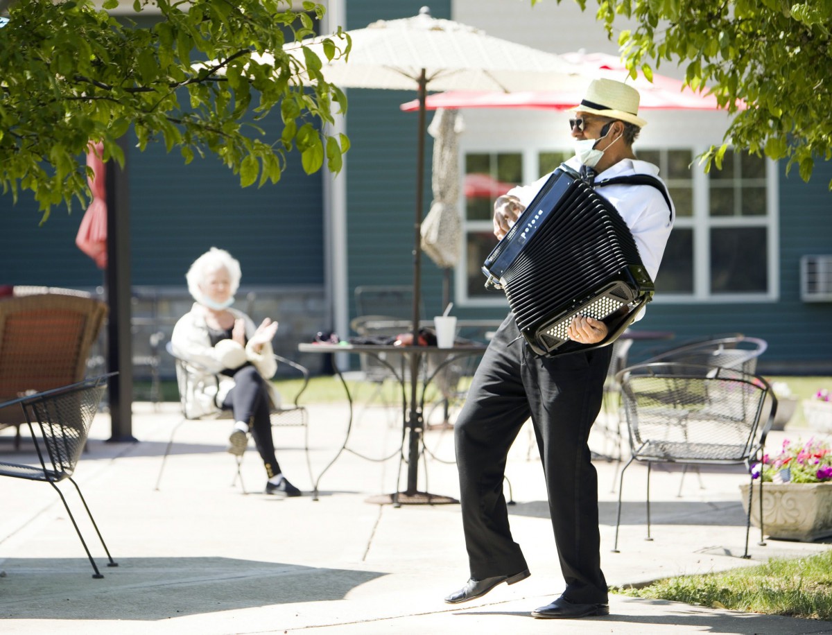 A musician plays the accordion on a sunny day while an audience member watches from a nearby table.