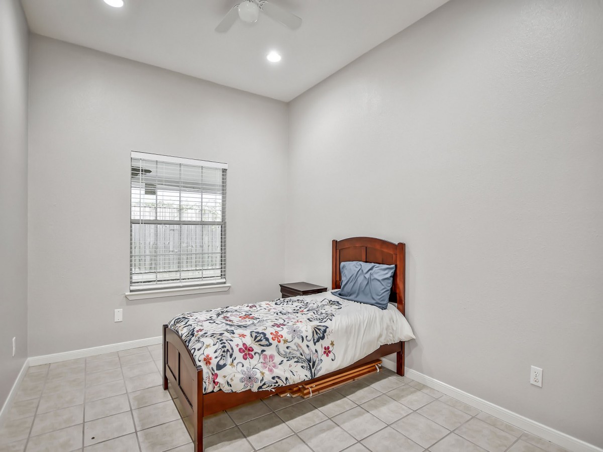 A minimalist bedroom with a single wooden bed and a large window, allowing natural light to fill the space.