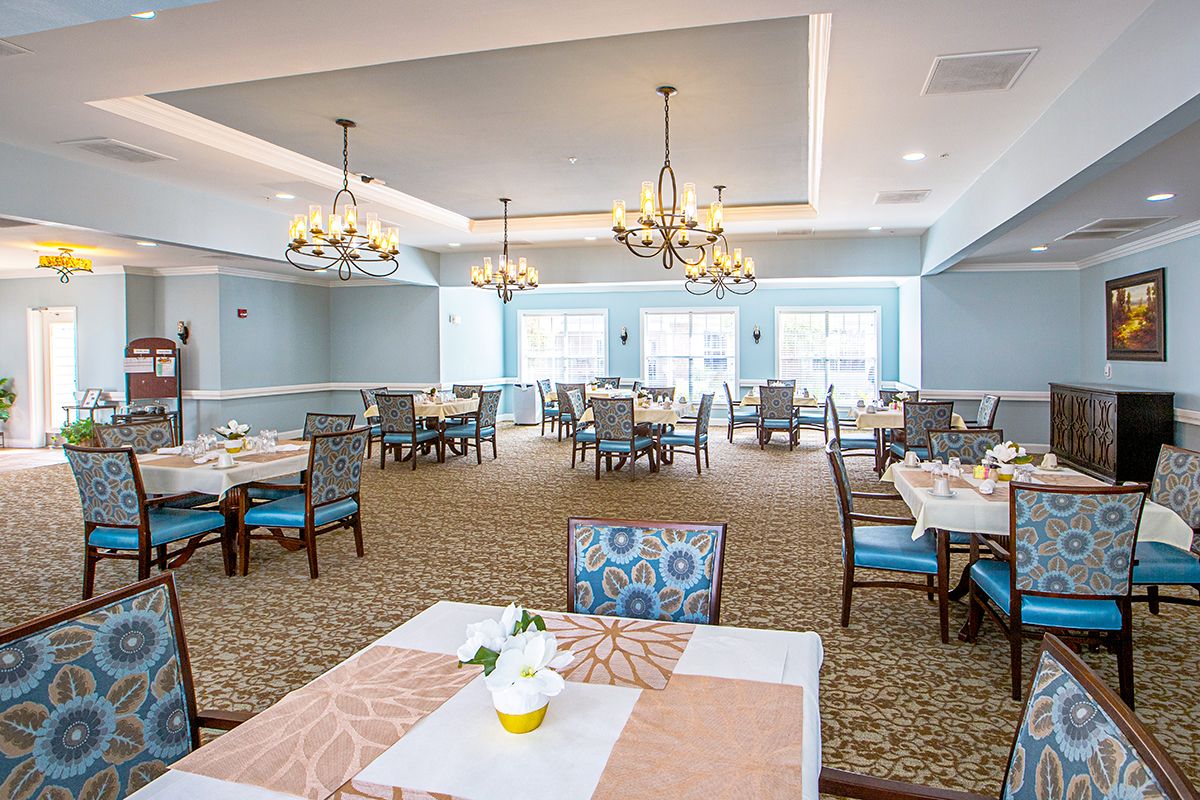 An elegant dining room with neatly arranged tables and chairs, illuminated by chandeliers.