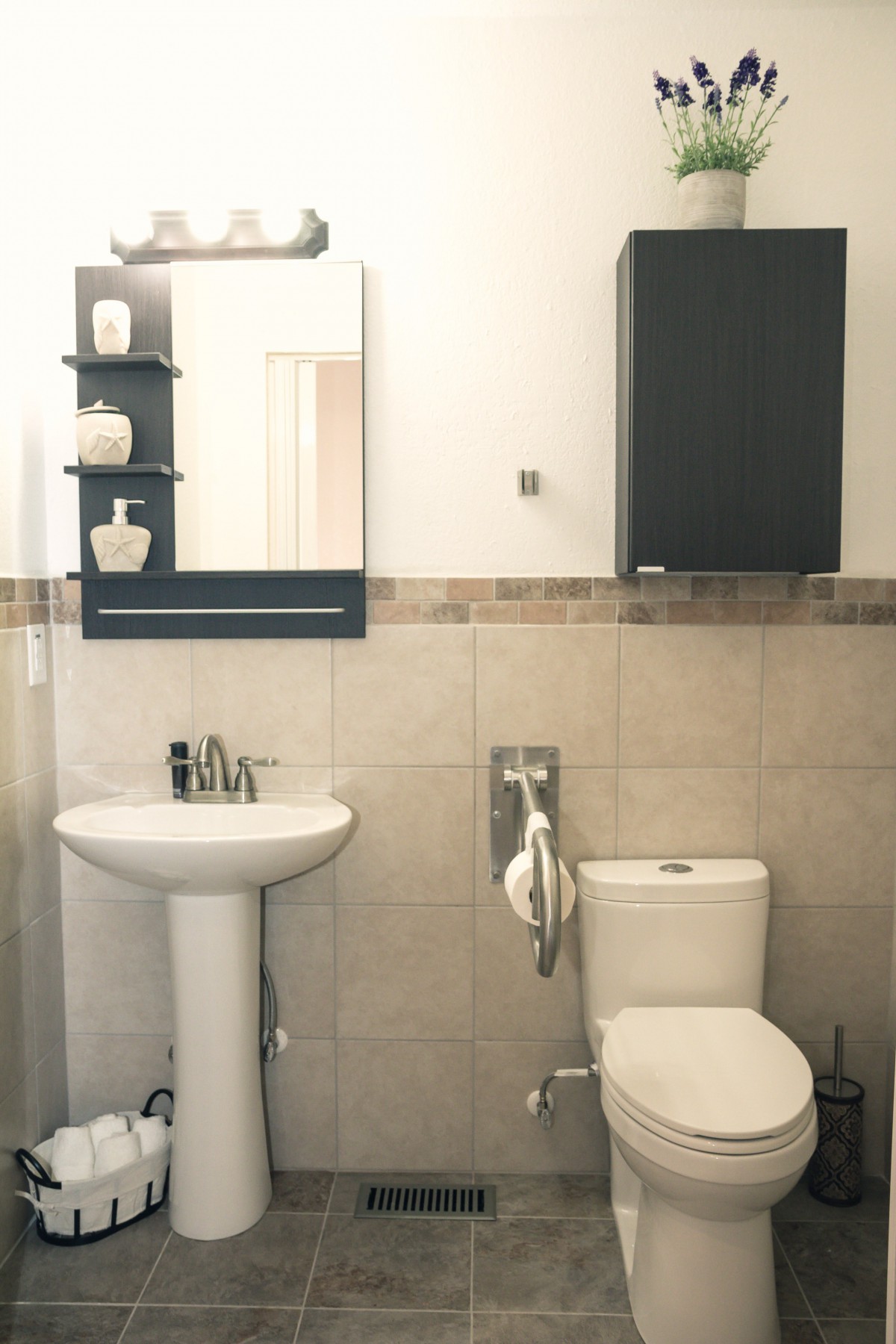 A modern bathroom with a pedestal sink, toilet, mirror, and black cabinet.