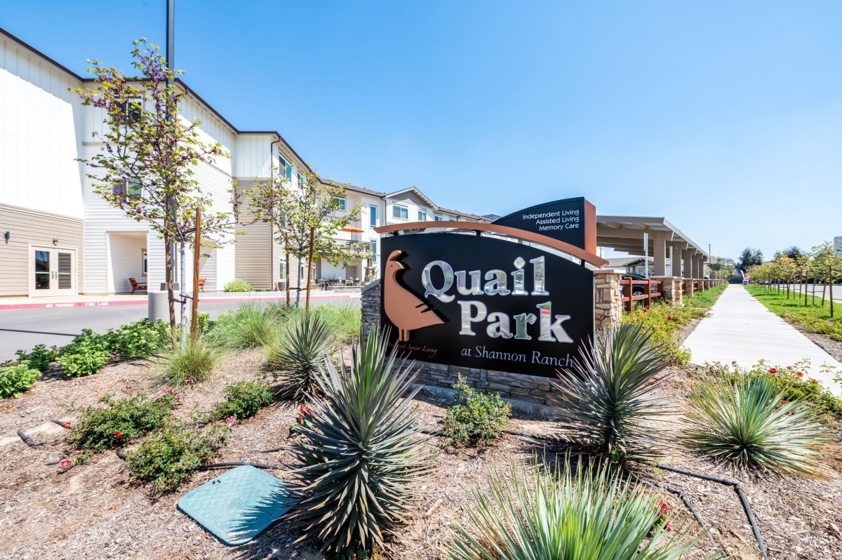 Entrance sign for Quail Park surrounded by landscaped greenery and residential buildings.