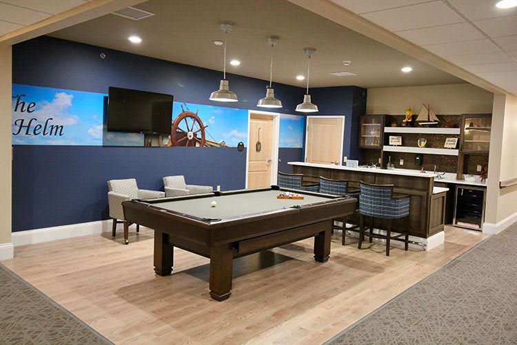 A modern game room featuring a pool table, bar seating, and a large TV.