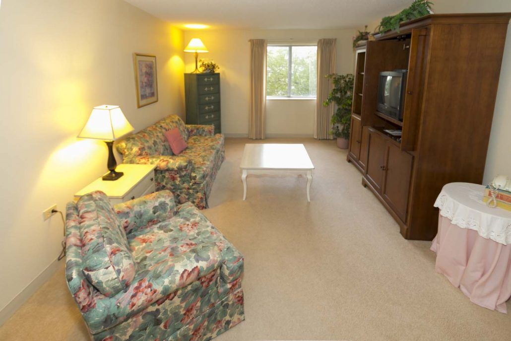 A cozy living room featuring a floral upholstered sofa, a wooden television cabinet, and a coffee table in the center.