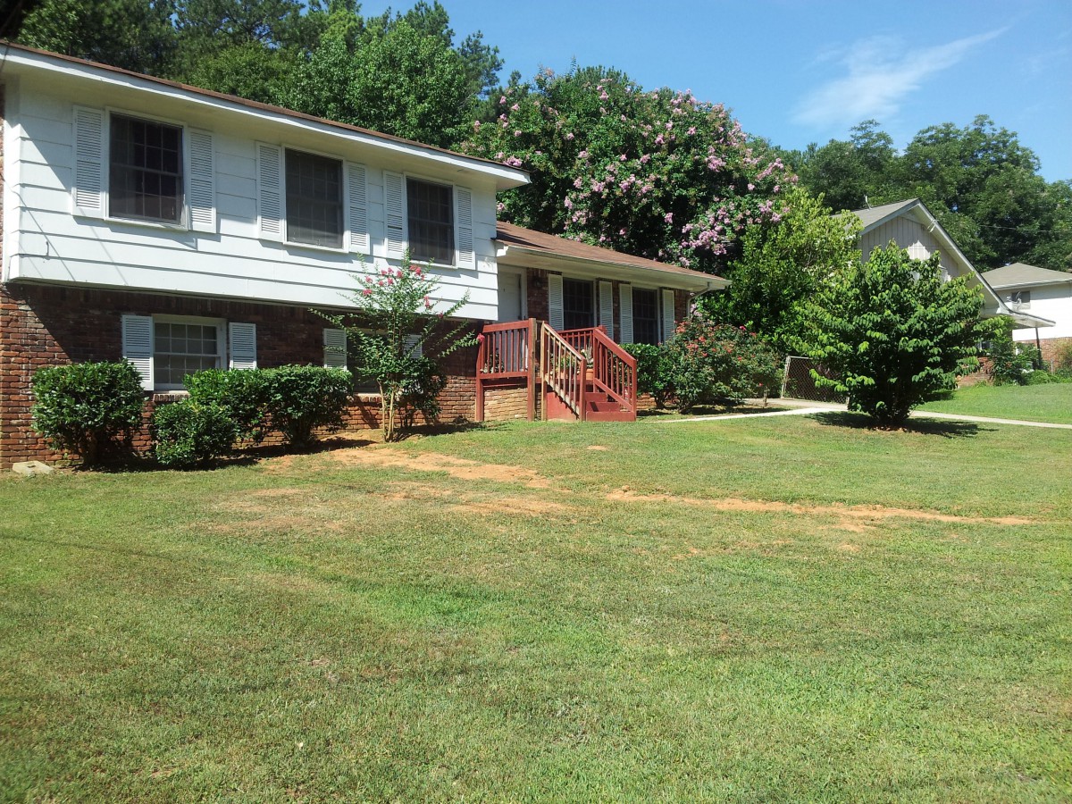 A suburban house with a well-maintained lawn and surrounded by trees on a sunny day.