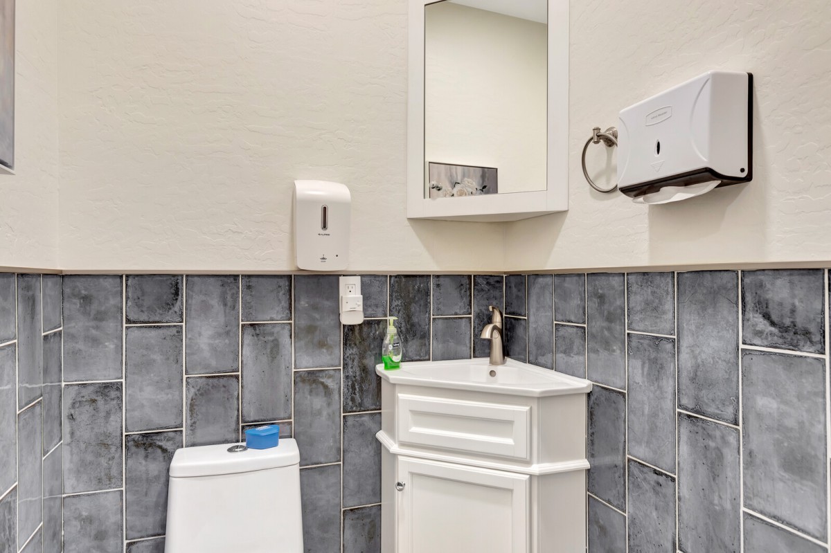 A compact bathroom with a sink, toilet, mirror, and wall-mounted hand dryer.