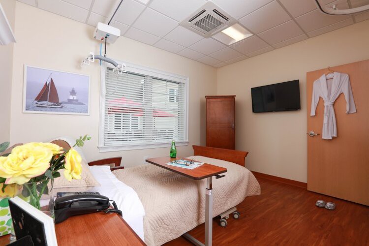 A clean and well-furnished hospital room with a bed, television, and window.