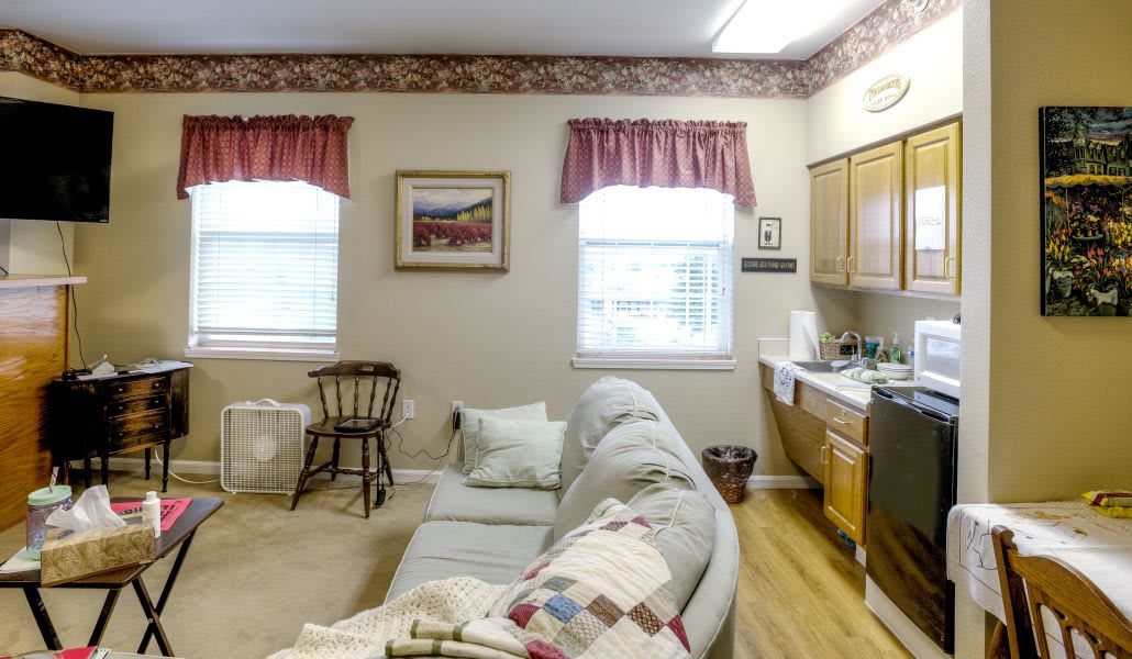 A cozy living room with a sofa and kitchenette, adorned with traditional decor and red curtains.