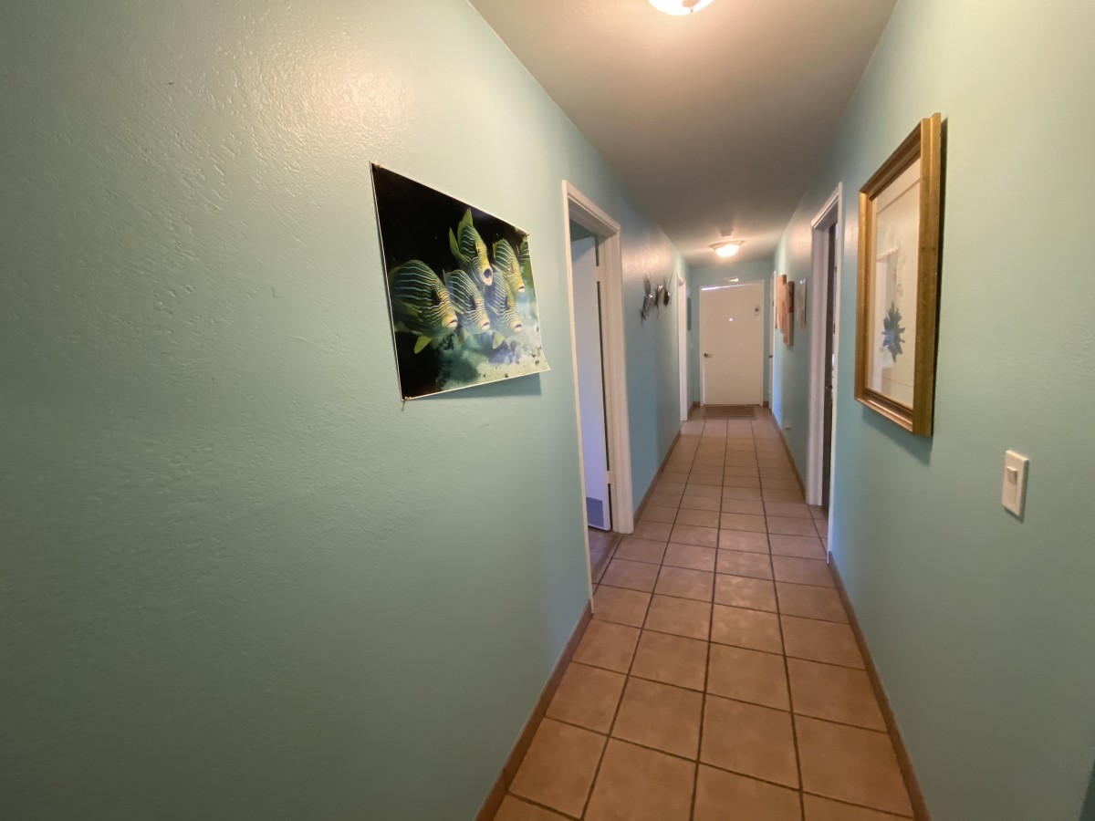 A hallway with tiled flooring, adorned with paintings and multiple doors along the walls.