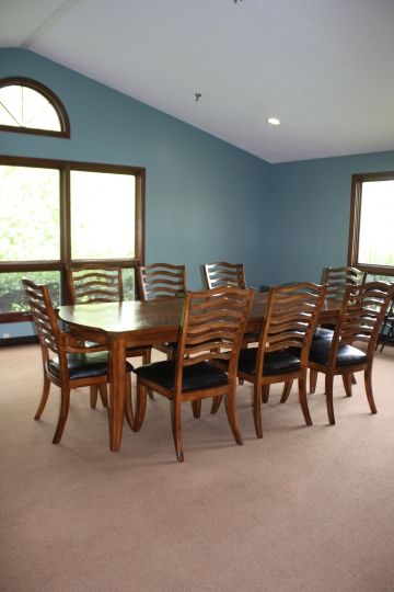 A spacious dining room with a wooden table and chairs, featuring large windows and blue walls.