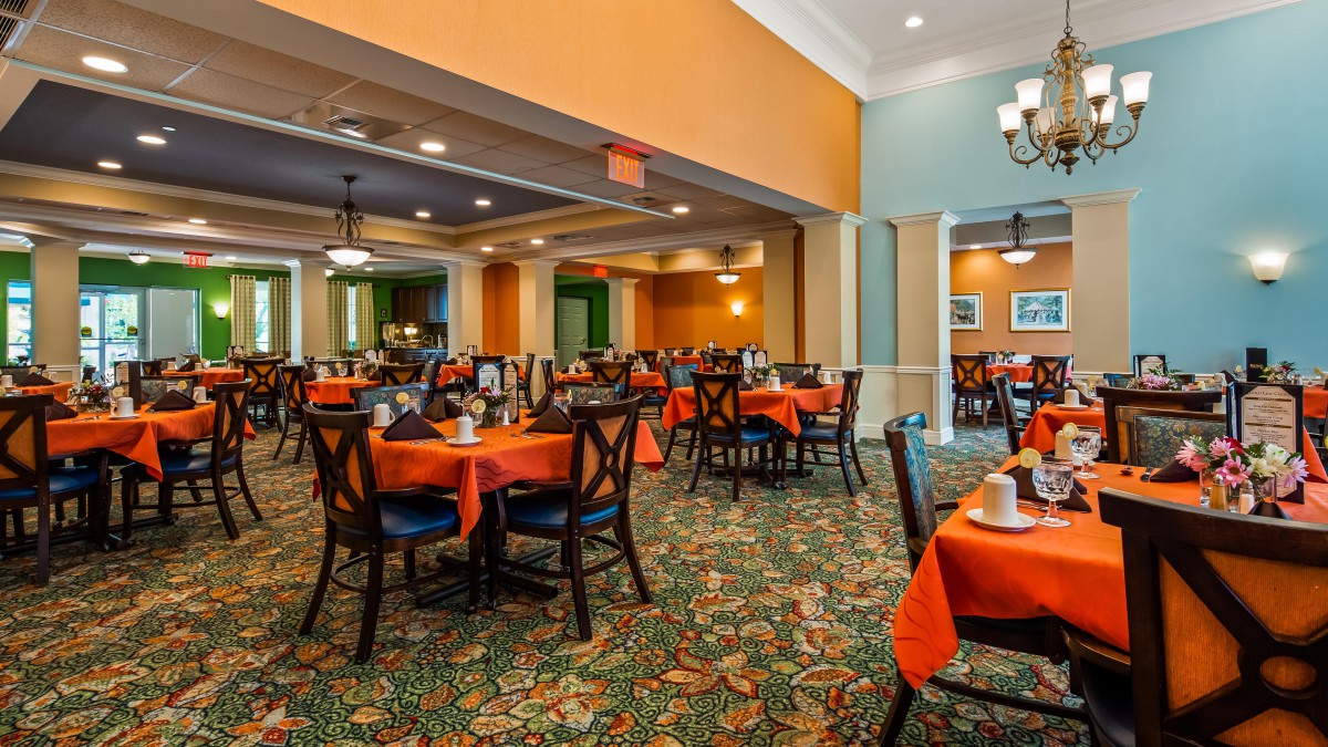 A spacious and elegantly decorated restaurant interior with orange tablecloths and neatly arranged seating.