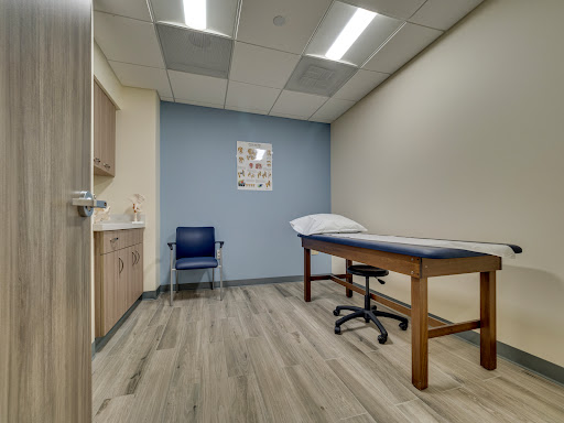 A clean and modern medical examination room, equipped with a treatment table and a chair for patients.
