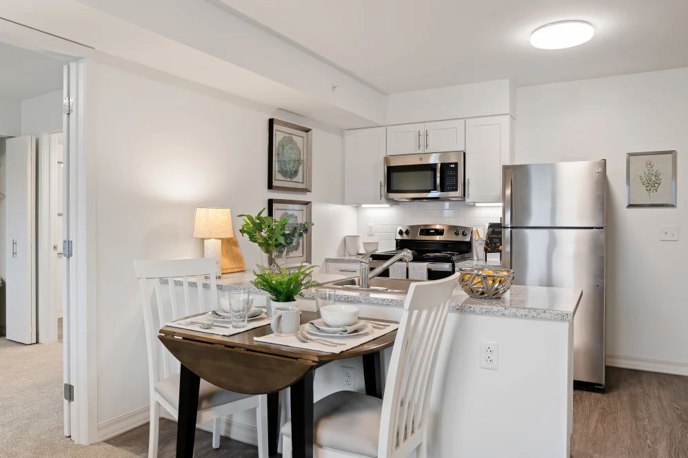 A modern kitchen with a small dining area featuring white cabinetry, stainless steel appliances, and a neatly set table.