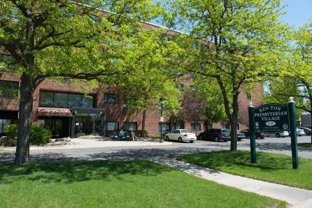 A sunny day in front of a brick building with trees and parked cars.