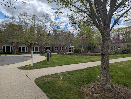 A serene outdoor space featuring a well-maintained pathway, lush greenery, and modern buildings under a partly cloudy sky.