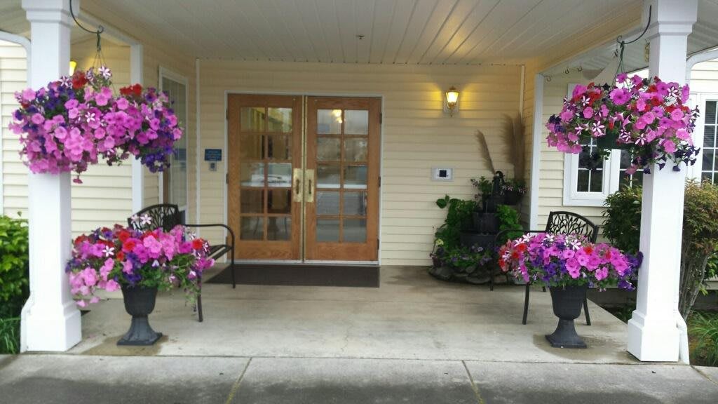 A welcoming entrance with double wooden doors, flanked by benches and potted flowers.