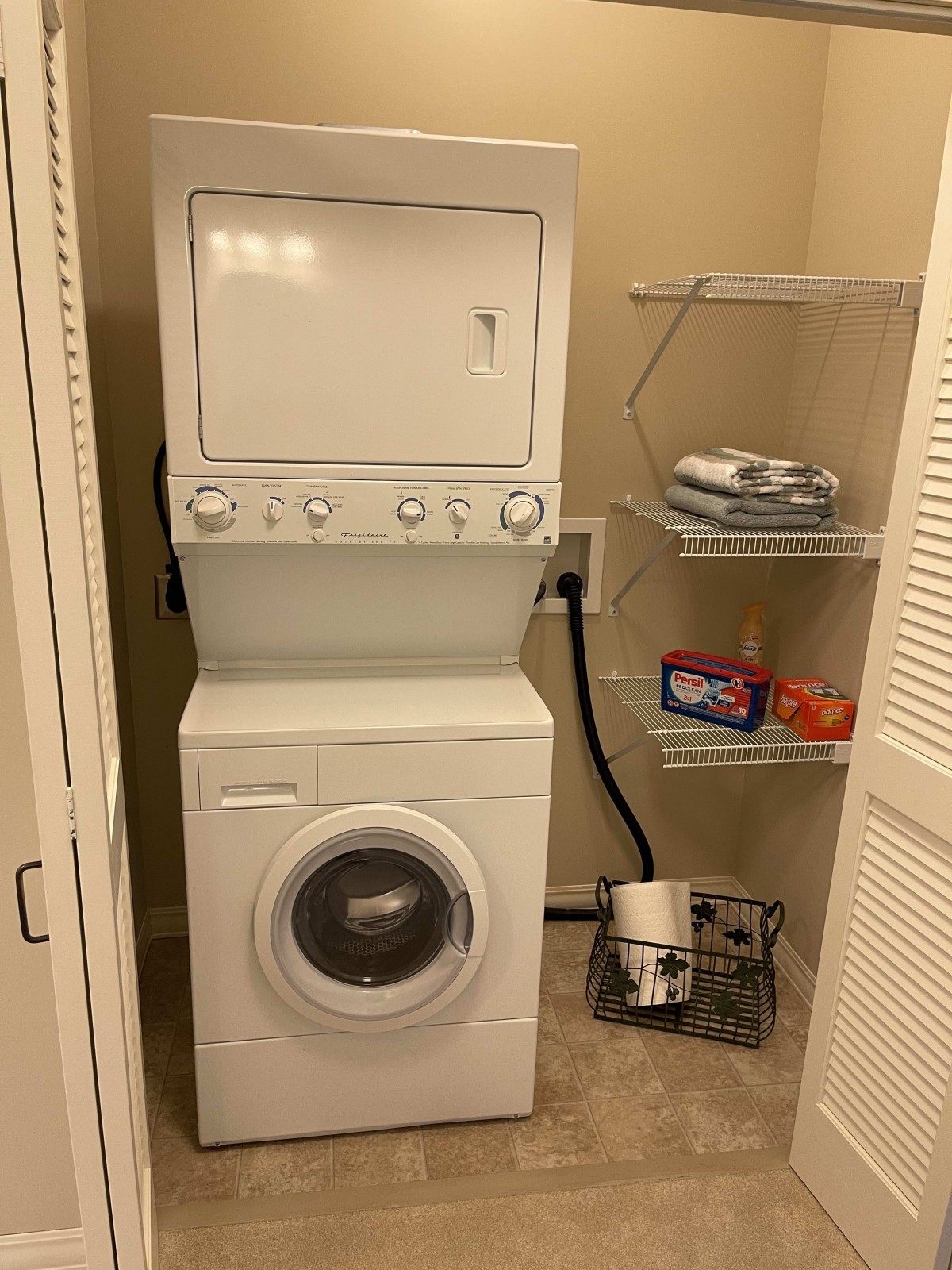 A compact laundry room with a stacked washer and dryer, alongside shelves holding laundry supplies.