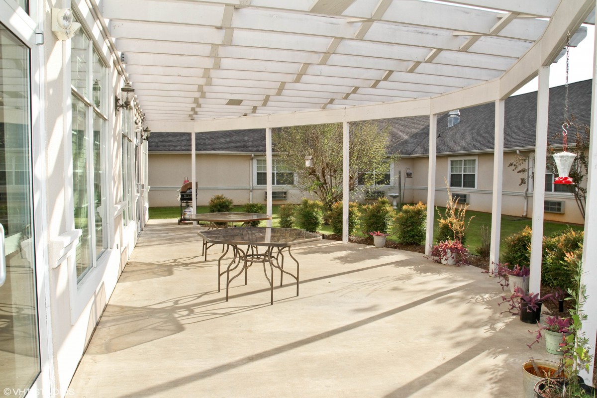 A sunny patio with outdoor furniture and a pergola, surrounded by greenery in a residential area.