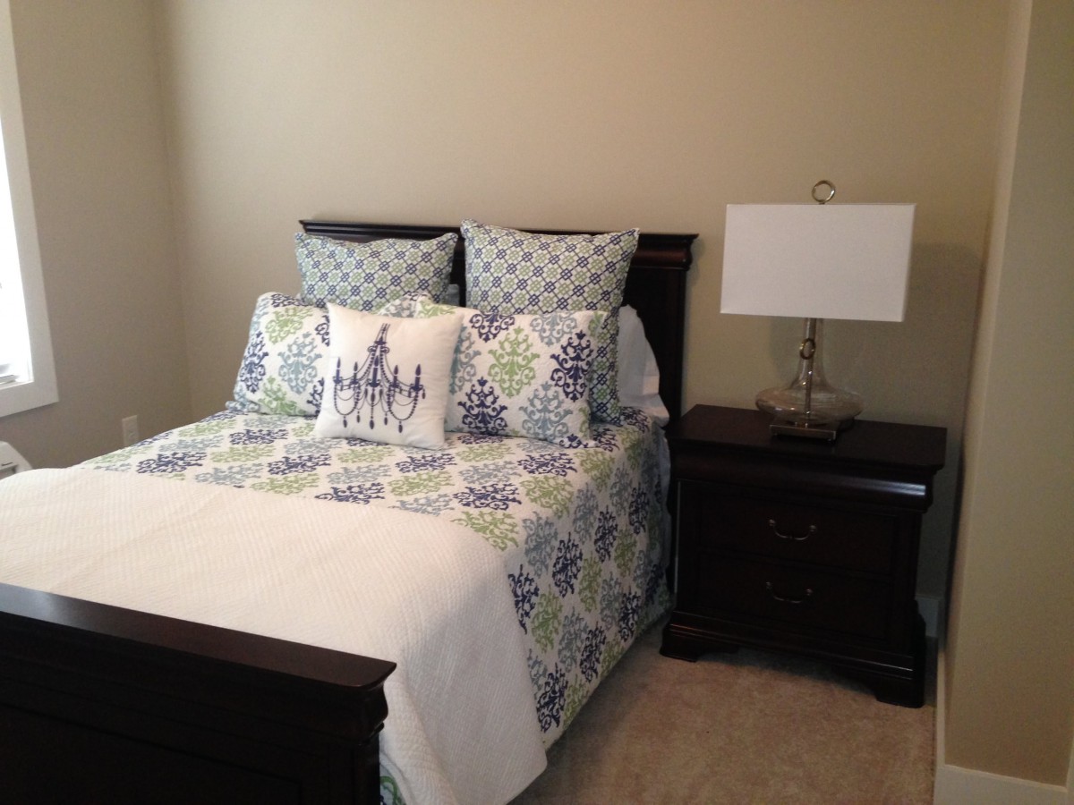 A neatly arranged bedroom with a bed, decorative pillows, and a nightstand with a lamp.