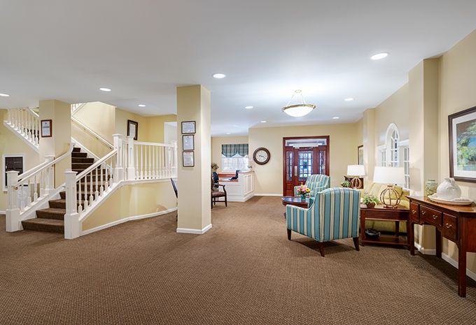 A warmly lit living area with carpeted flooring, featuring a cozy seating arrangement and a staircase.