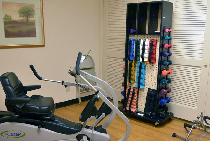 A small gym area featuring a stationary bike and a rack of colorful dumbbells.