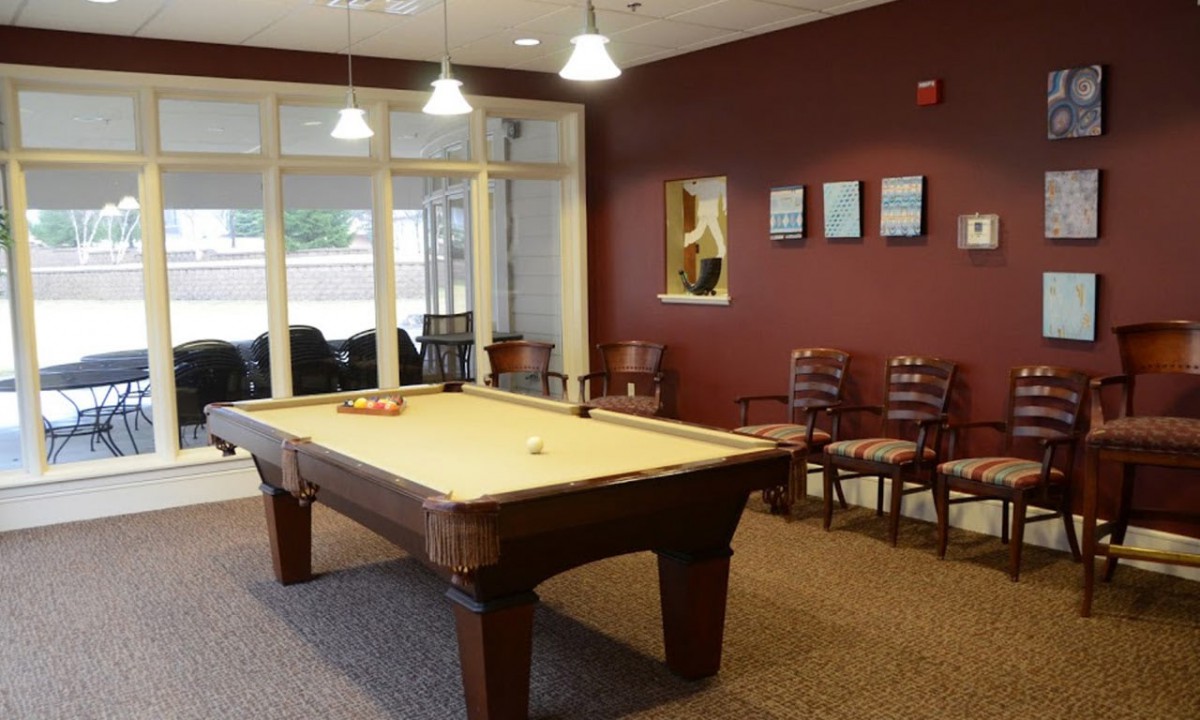 A cozy billiards room with a pool table, surrounded by chairs and decorated with paintings.