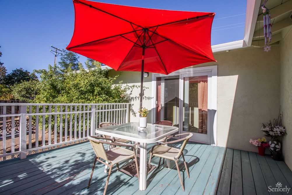A sunny outdoor deck with patio furniture and a vibrant red umbrella.