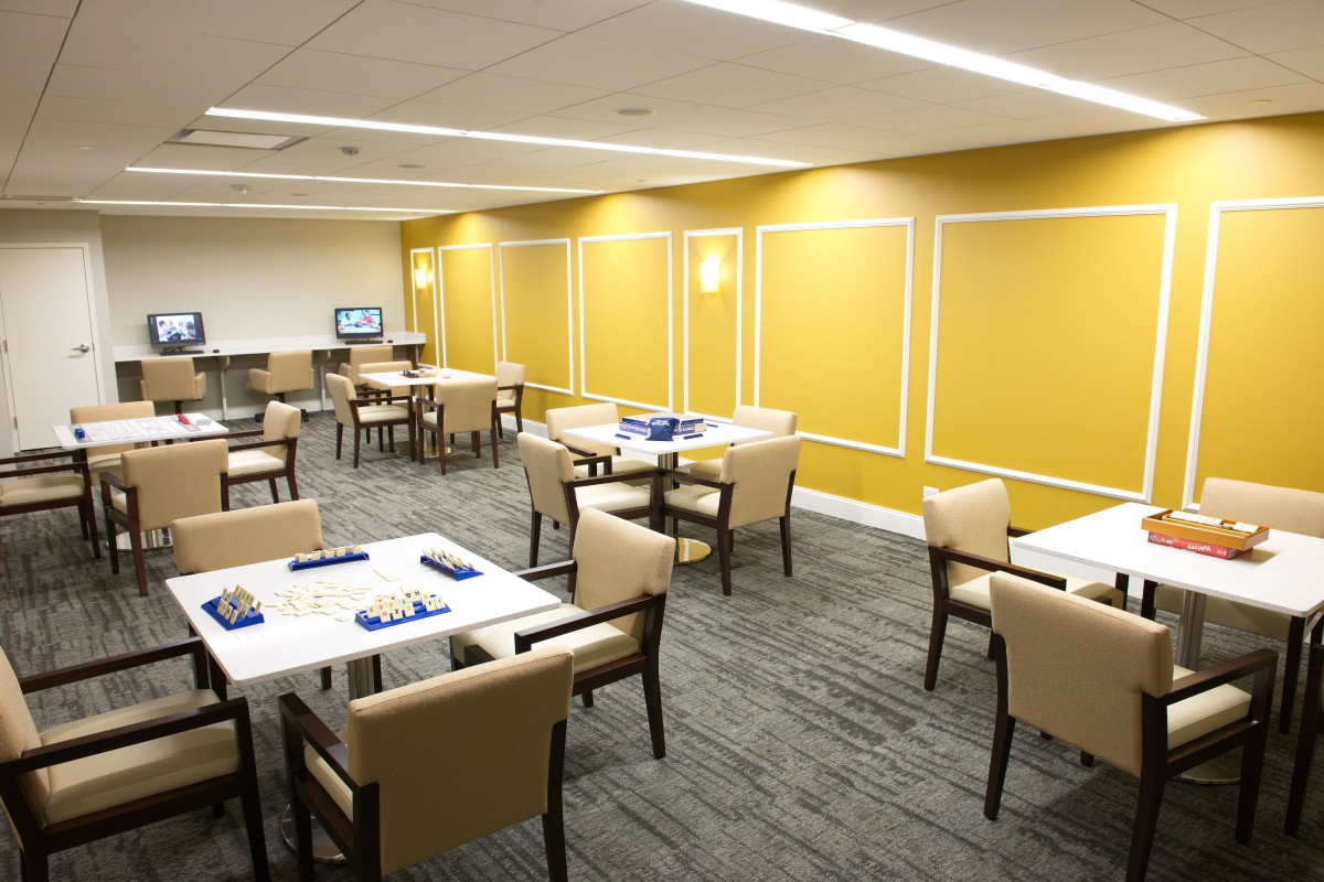 A modern dining area with neatly arranged tables and chairs, featuring vibrant yellow walls and a carpeted floor.