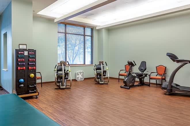 A spacious gym room featuring exercise machines and wooden flooring.
