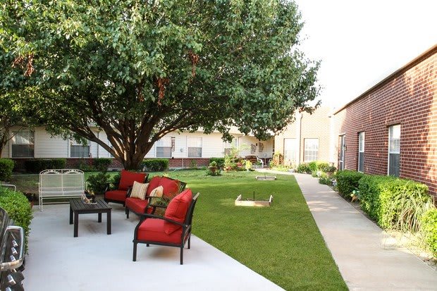 A peaceful backyard with a large tree, patio furniture, and a grassy lawn.