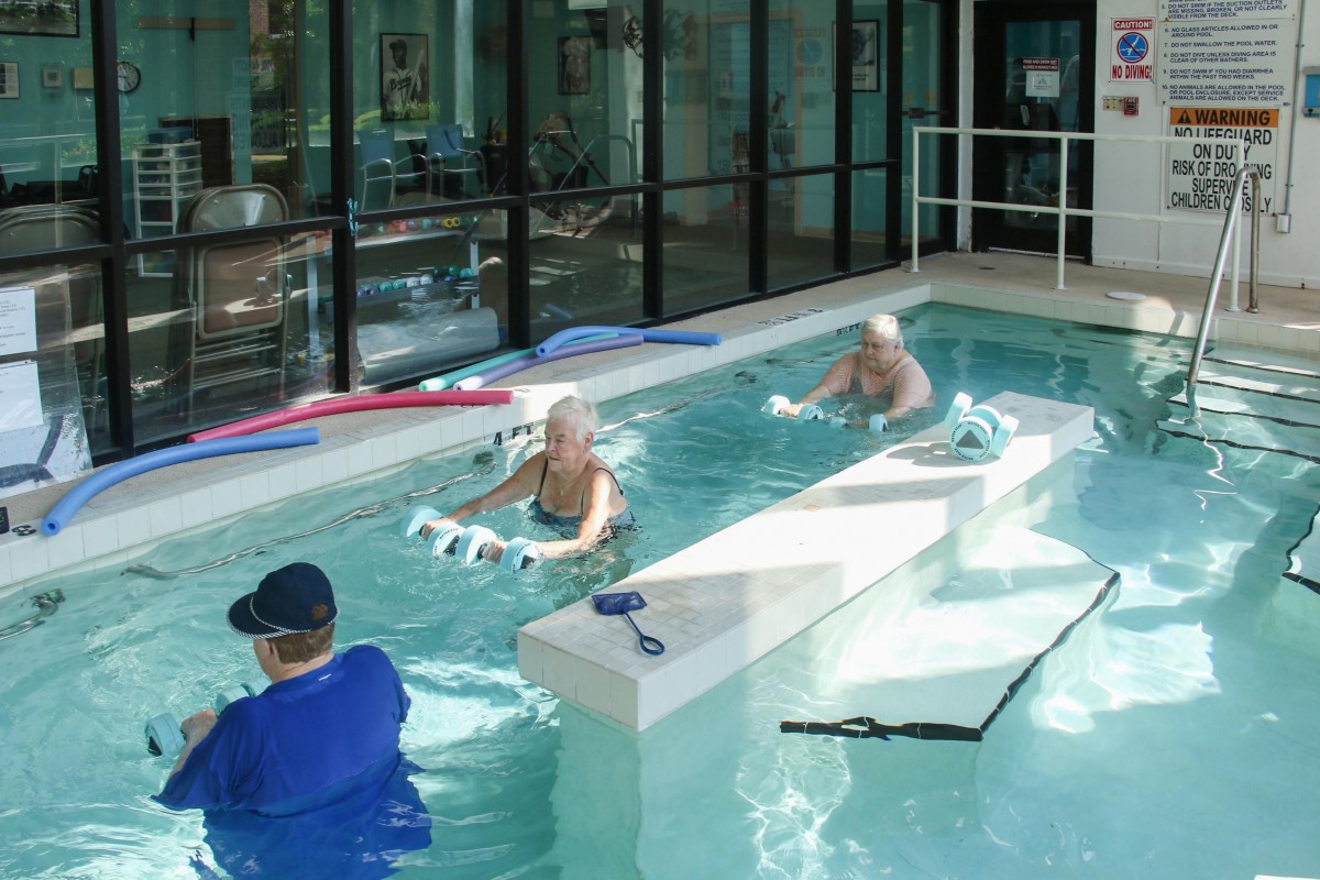 A group of seniors participating in aquatic therapy exercises in an indoor pool.