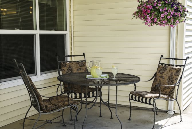 A cozy patio setting with a metal table, three chairs, and a pitcher of lemonade, complemented by a hanging plant.