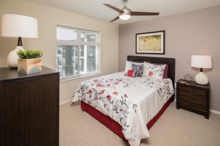 A cozy bedroom with a floral bedspread, accented by a large window and ceiling fan.