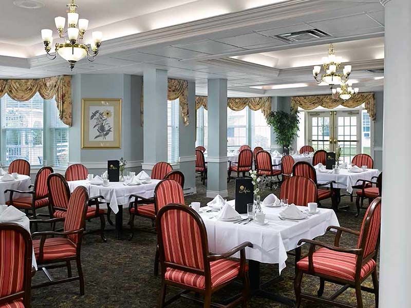 An elegant restaurant dining room with neatly arranged tables and chairs, adorned with chandeliers.