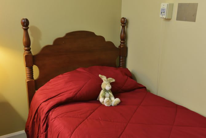 A cozy bedroom featuring a single bed with a red bedspread and a stuffed animal placed on it.
