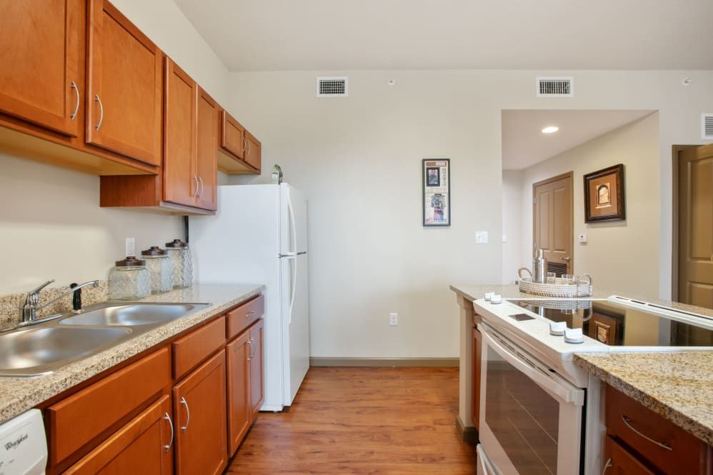 A cozy kitchen with wood cabinets, a refrigerator, and a stove, featuring wood flooring.
