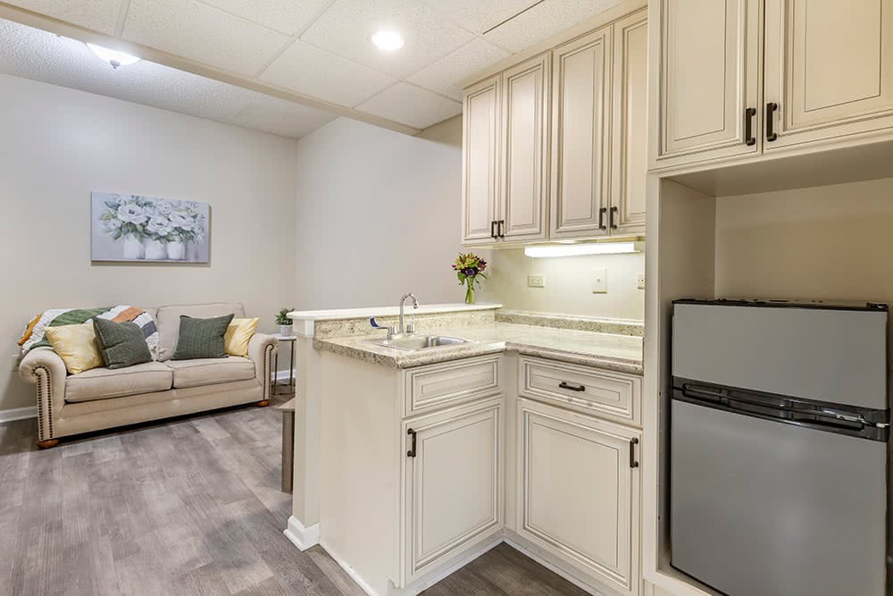 A modern kitchen with cream cabinets and a compact living area in the background.