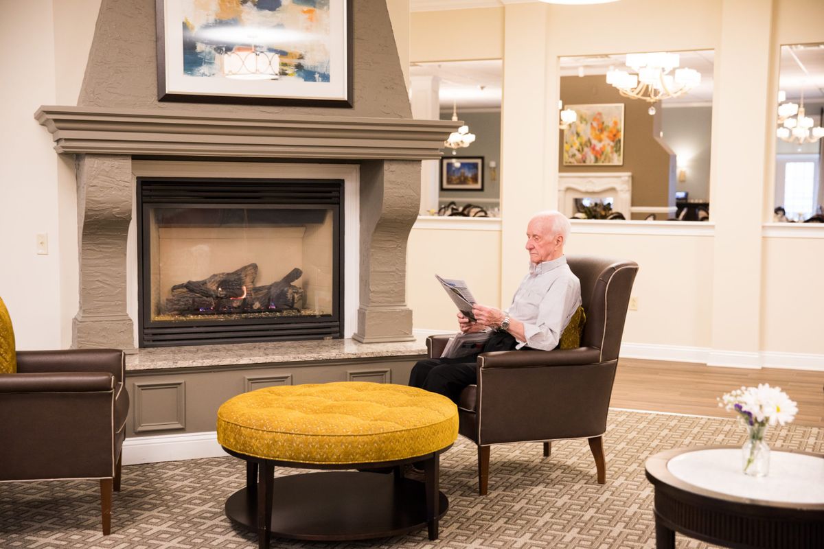 A cozy living room with a fireplace and a person reading in an armchair.