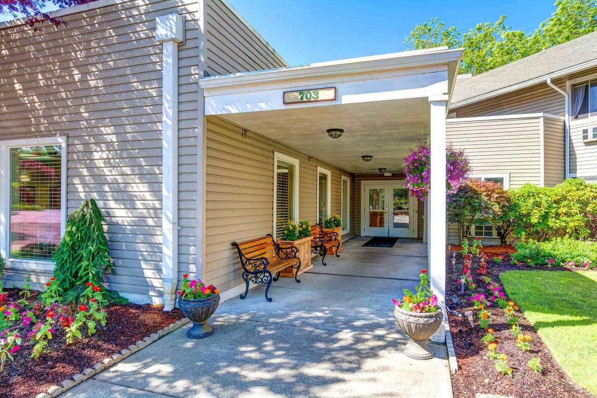 A welcoming building entrance with benches and vibrant landscaping.