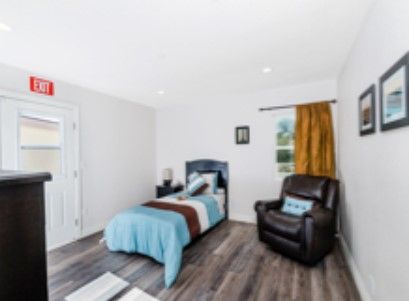 A cozy, minimalist bedroom features a single bed with blue bedding and a leather armchair.