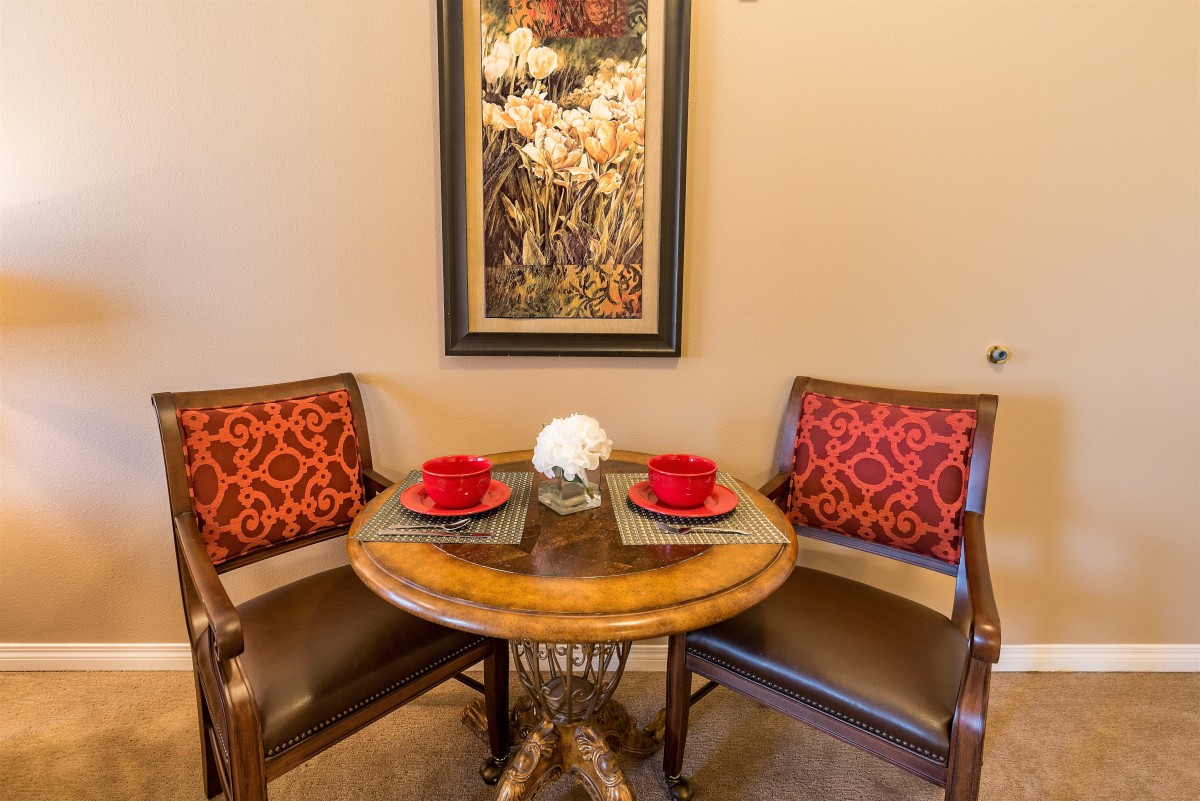 A cozy dining nook with a round wooden table, two chairs featuring red cushions, and wall art adding an elegant touch.
