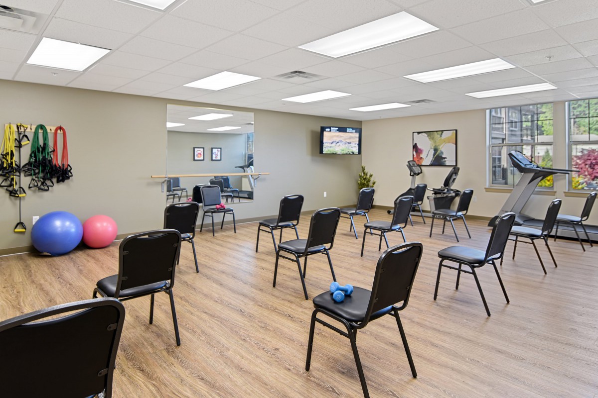 An exercise room with chairs arranged for a fitness class, featuring mirrors and gym equipment.