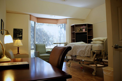 A spacious hospital room featuring a bed, seating area, and natural light streaming through the window.