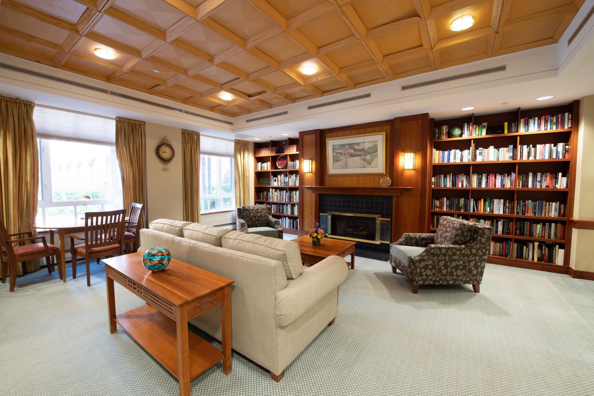 A cozy living room with a fireplace, surrounded by bookshelves and comfortable seating.