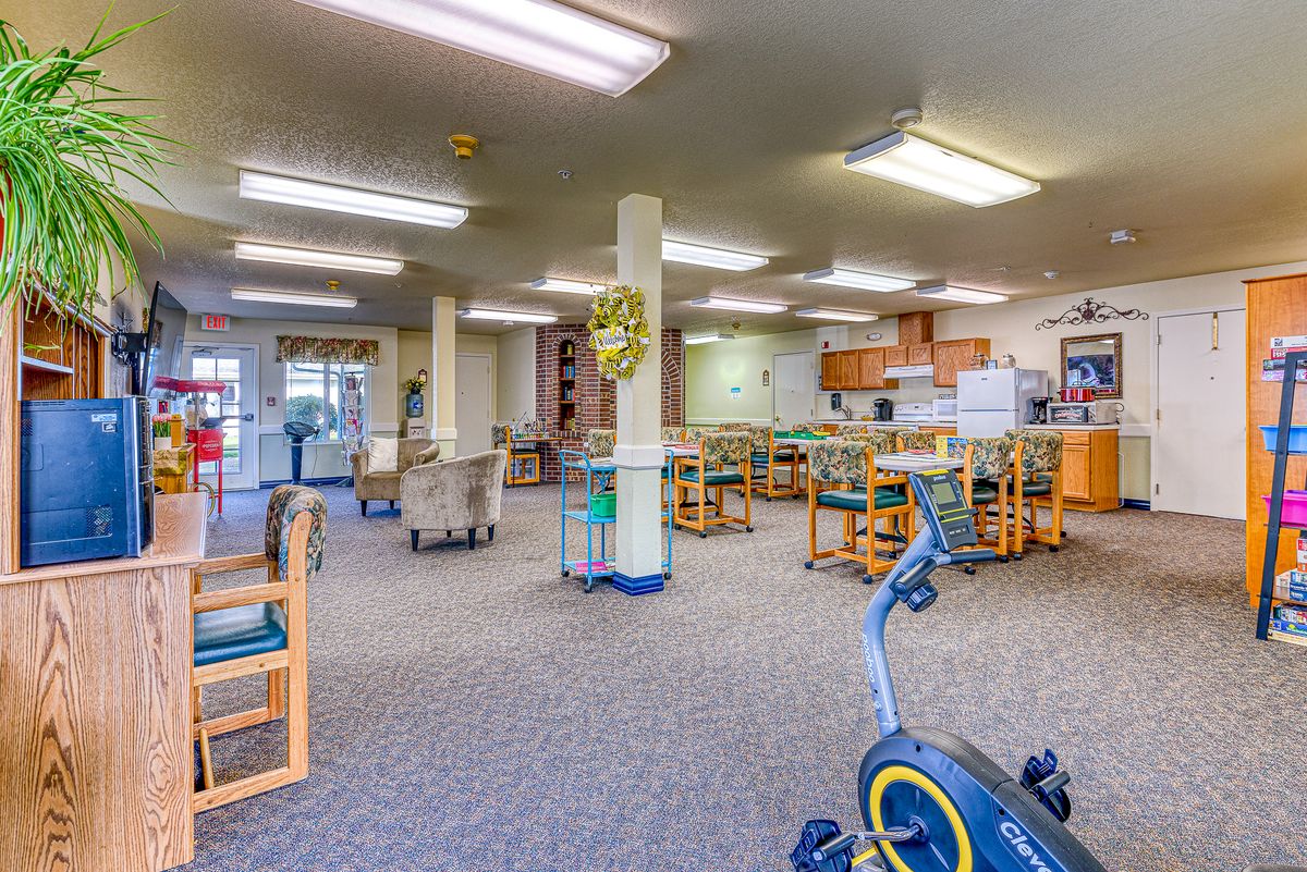 A spacious room with exercise equipment, tables, and chairs under fluorescent lighting.