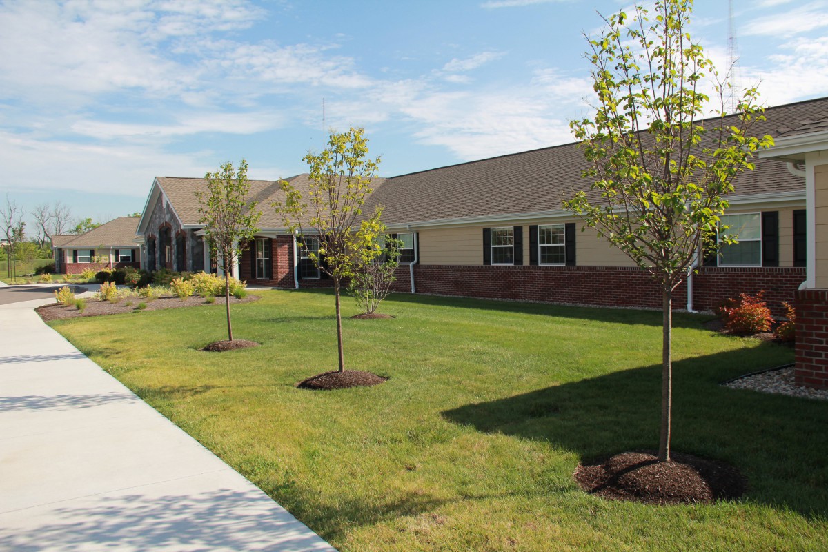 A sunny day at a building with a well-maintained lawn and young trees along a sidewalk.