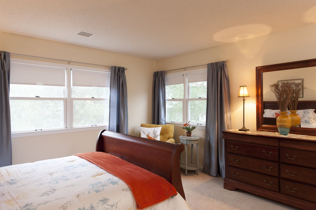 A cozy bedroom with a wooden bed, soft lighting, and large windows adorned with blue curtains.