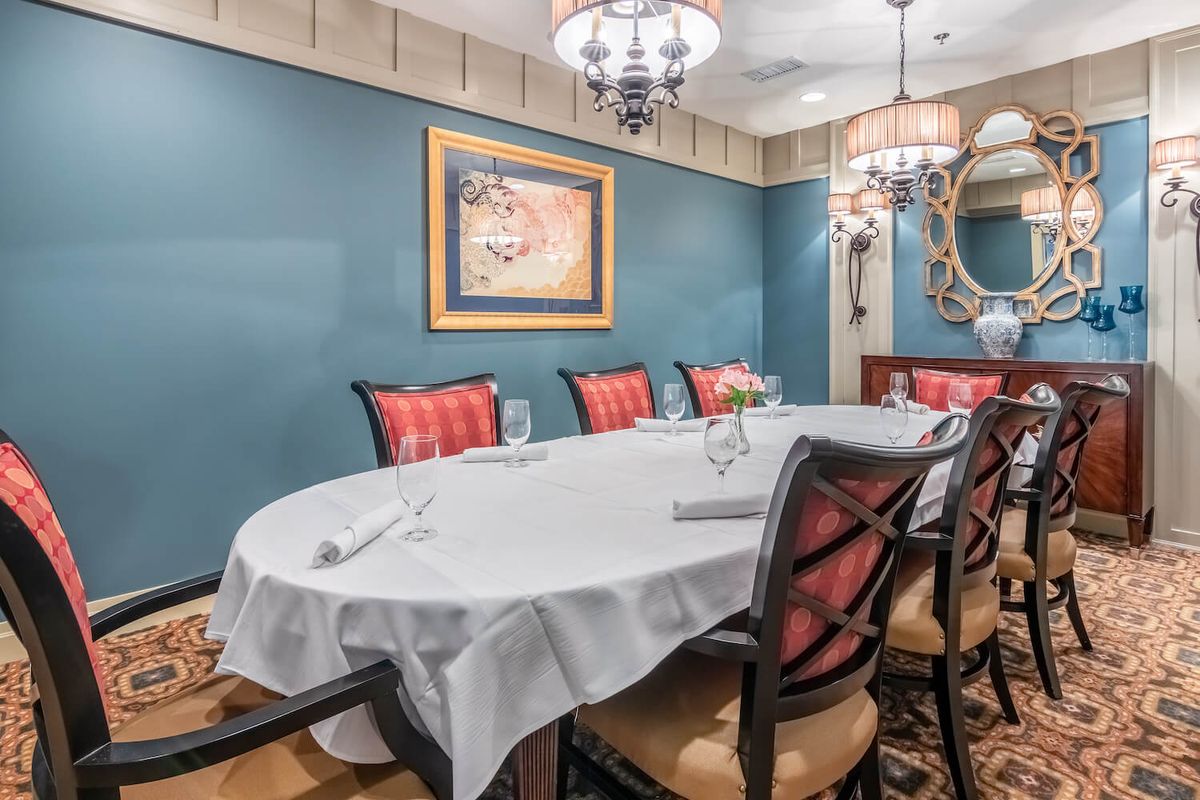 An elegantly set dining room featuring a large oval table, cushioned chairs, and decorative chandeliers.