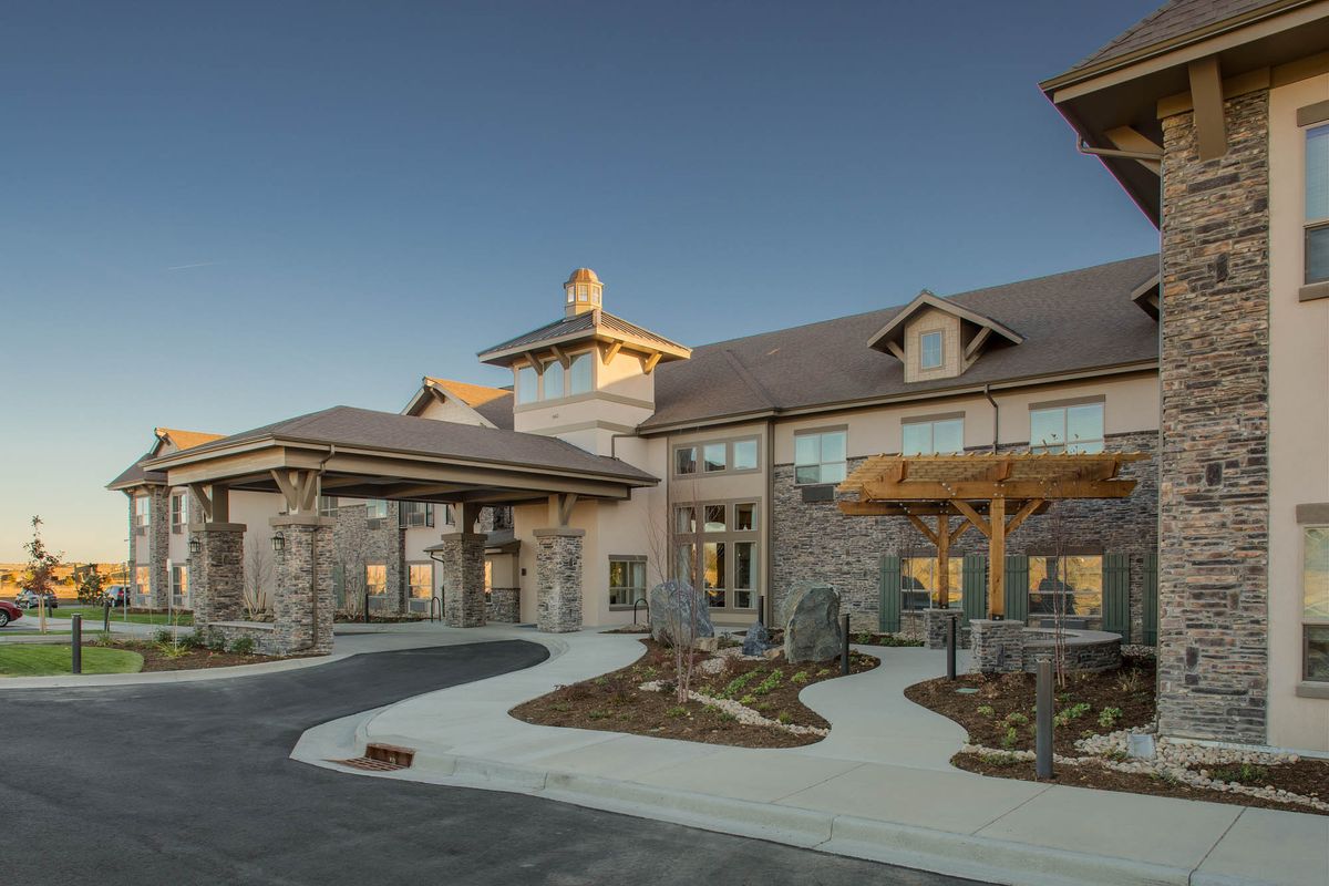 A modern building with a stone exterior and landscaped driveway under a clear sky.