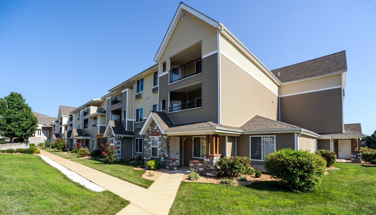 A modern apartment building on a sunny day with a well-maintained lawn and walkway.