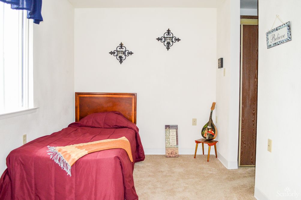 A minimalist bedroom with a single bed featuring red bedding, decorative wall art, and a small side table.